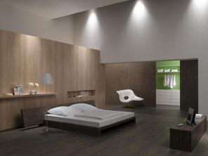 Schlafzimmerimpression von Bett, Nachtisch und Sideboard mit Holzverkleidung an Wand und indirektert Beleuchtung