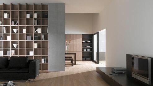 Offene Wohnraumimpression mit Einbauregal für Bücher und Dekoration in Trennwand mit hellem Holzboden